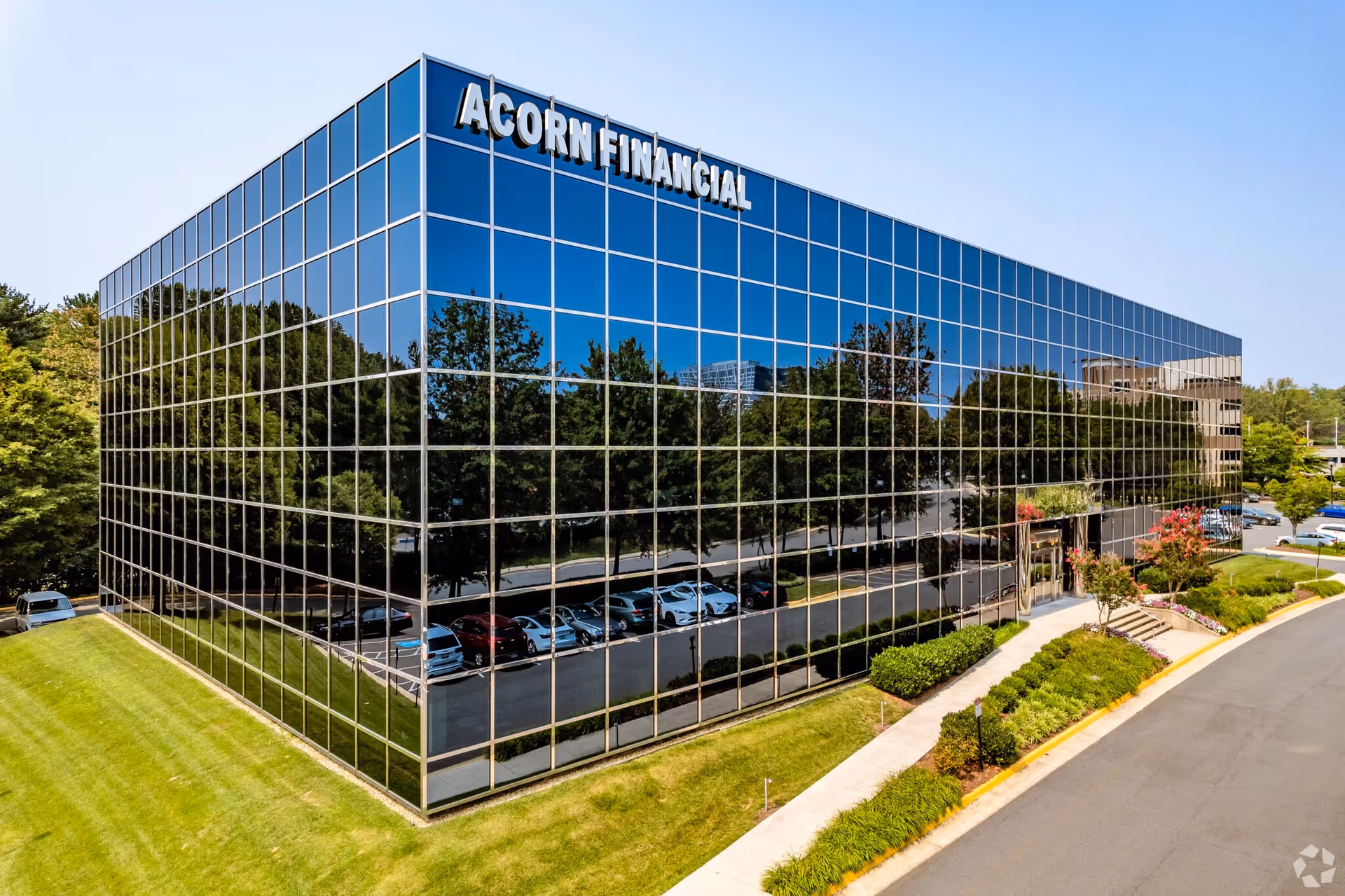 A reflective glass office building with ACORN FINANCIAL signage, surrounded by trees and a parking lot.