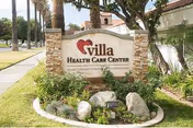Exterior view of Villa Health Care Center sign with landscaping and palm trees.