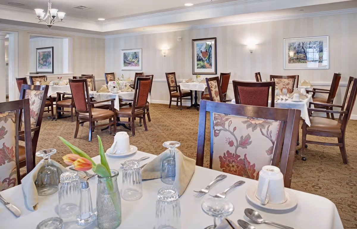 Dining room with neatly set tables, floral-upholstered chairs, and framed artwork on the walls.