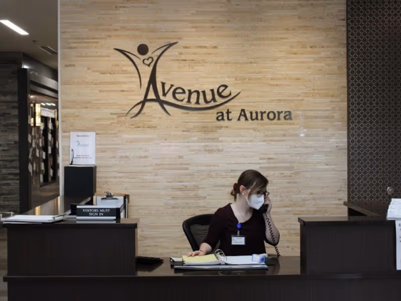 Reception desk with a masked staff member on the phone beneath an 'Avenue at Aurora' wall sign.