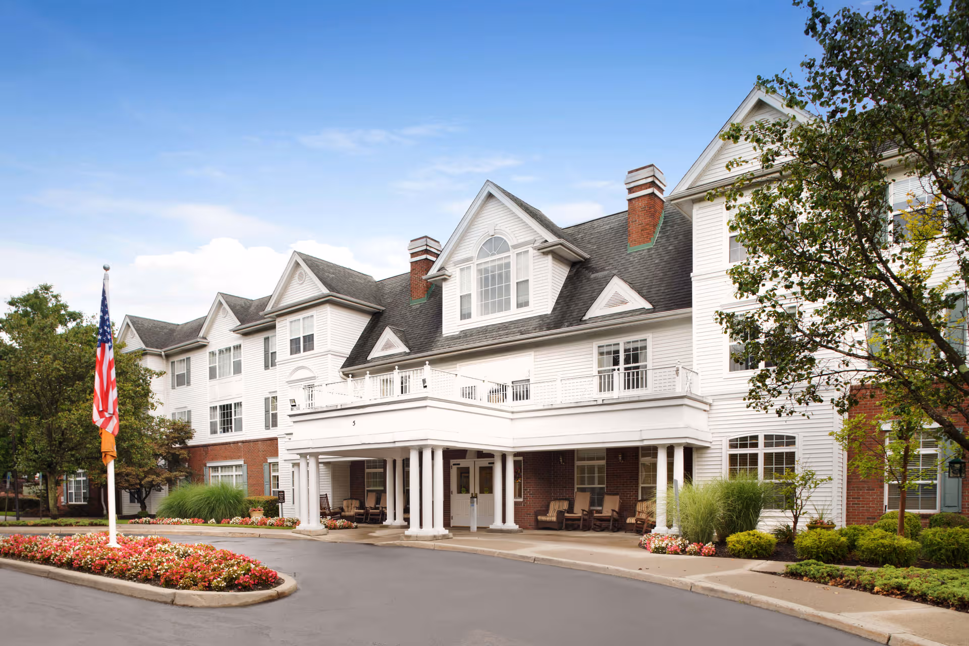 White multi-story senior living building with a covered entrance and landscaped front yard.