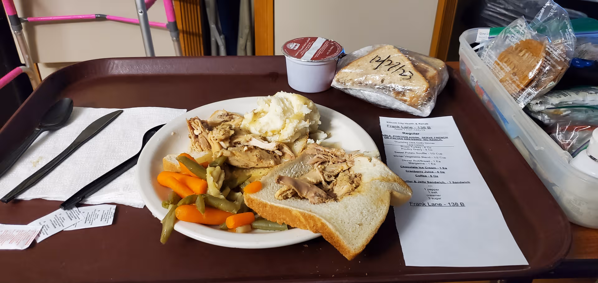 Tray with sandwich, vegetables, and dessert on a dining table inside a senior living facility.