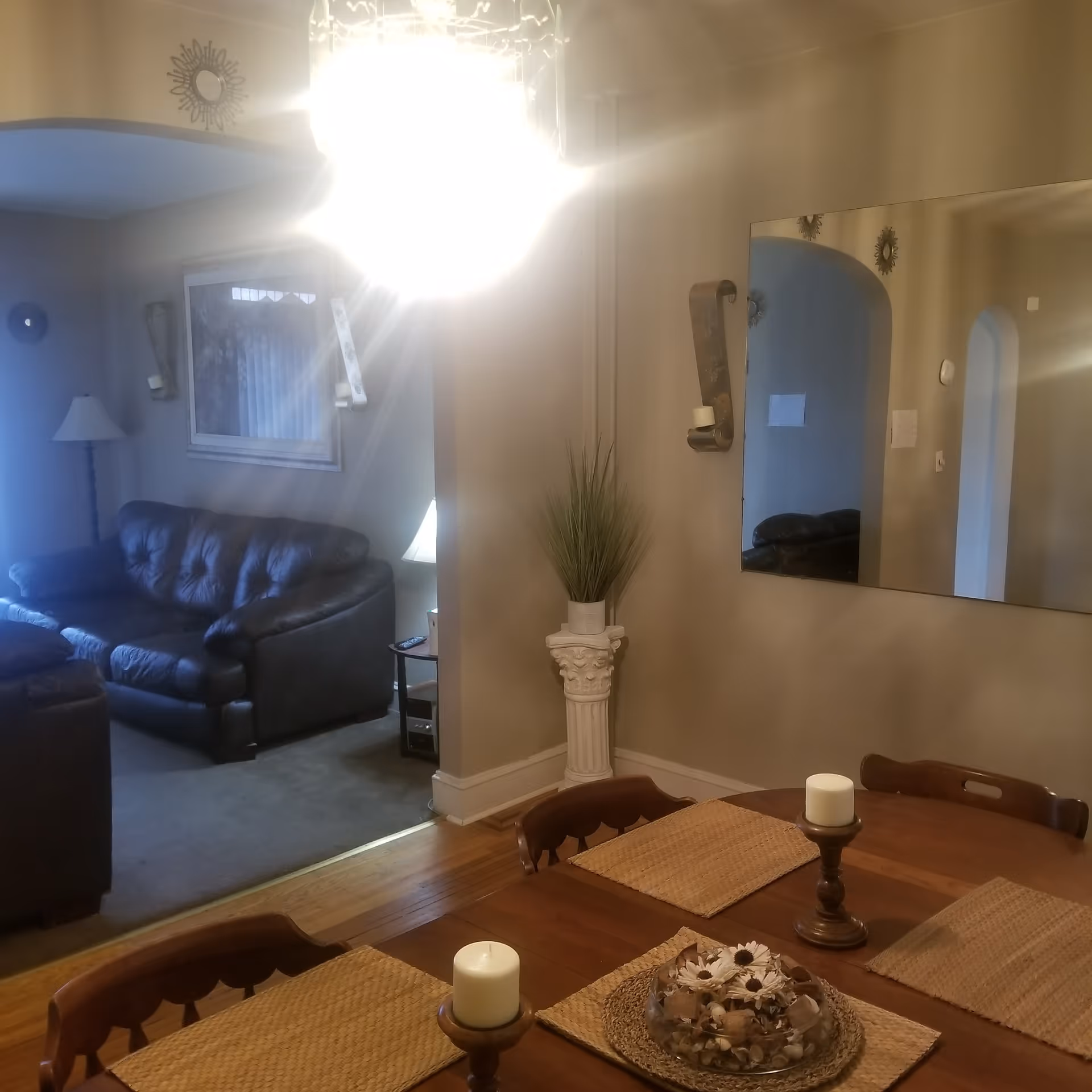 Dining room with wooden table, candles, and a mirror, adjacent living area.