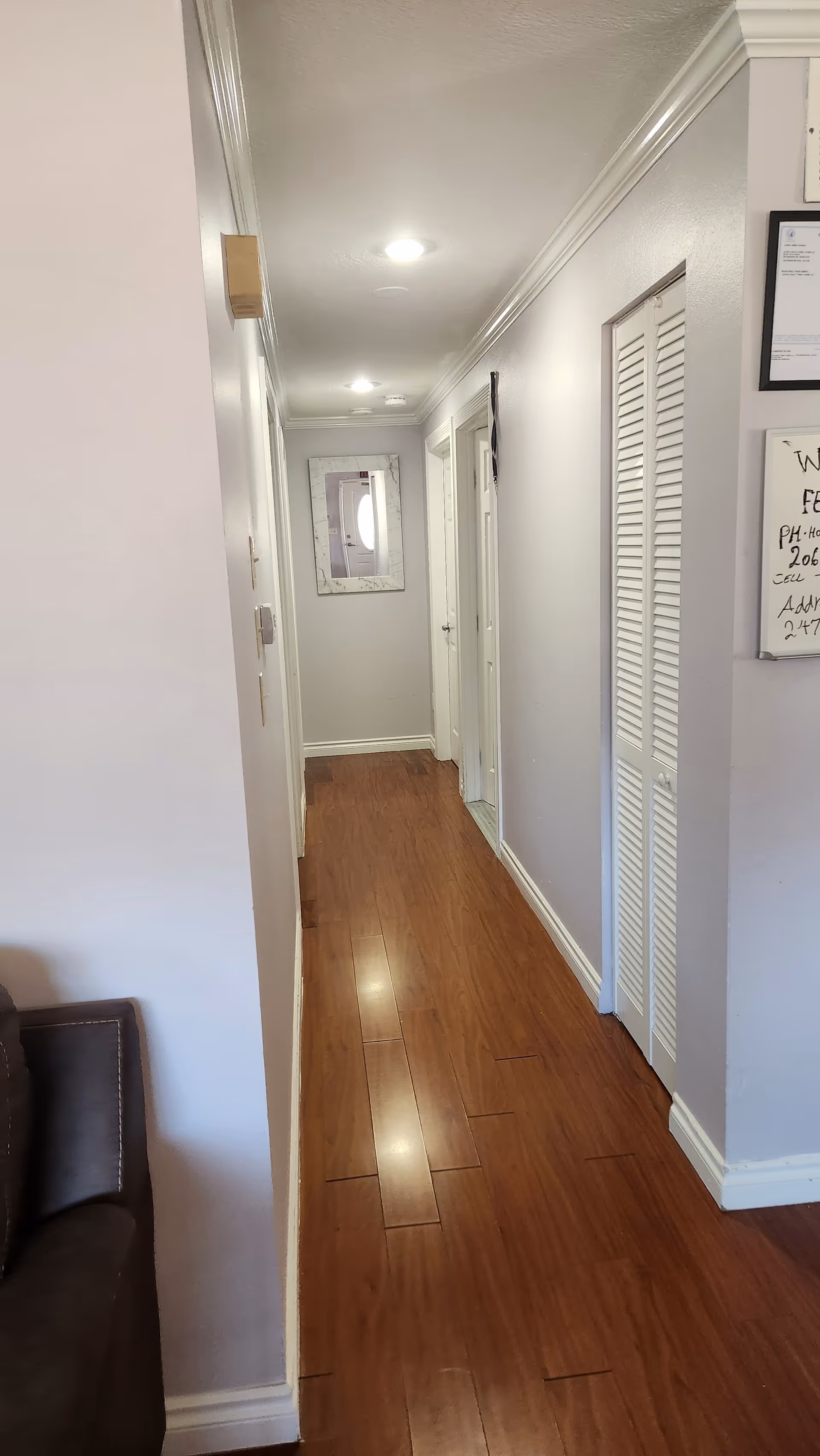 A narrow hallway in a senior living facility with wood floors, framed art, and doors.