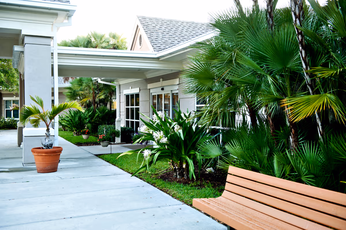 Outdoor entrance with a bench and tropical plants at Solaris Healthcare Charlotte Harbor.
