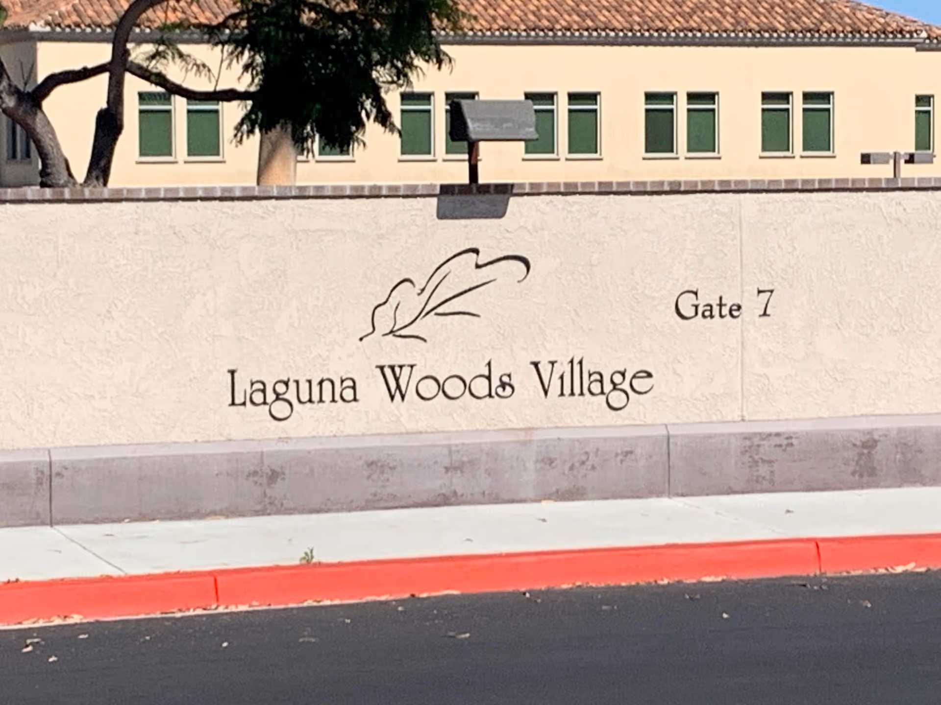 Laguna Woods Village sign on exterior wall with Gate 7 and building windows behind
