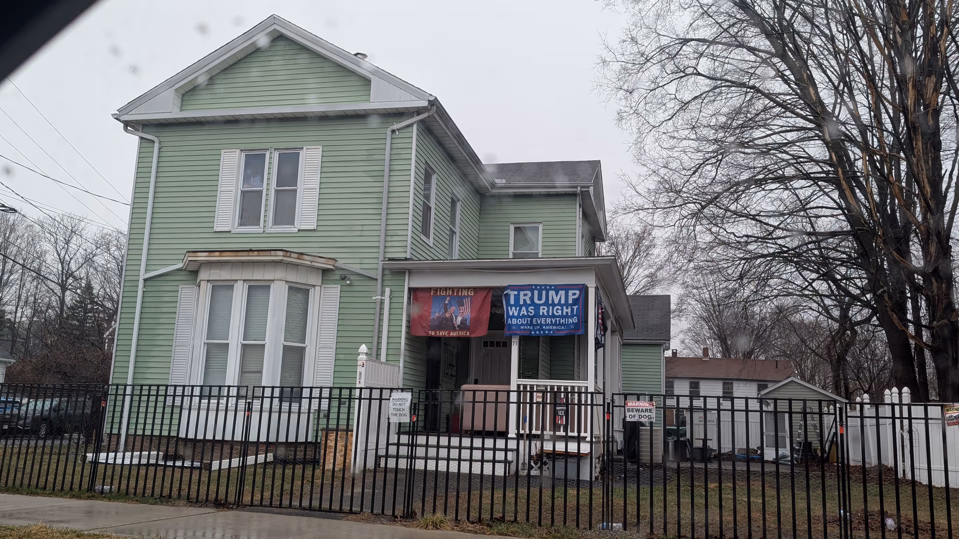 Green two-story house-style building with banners and a metal fence in front.