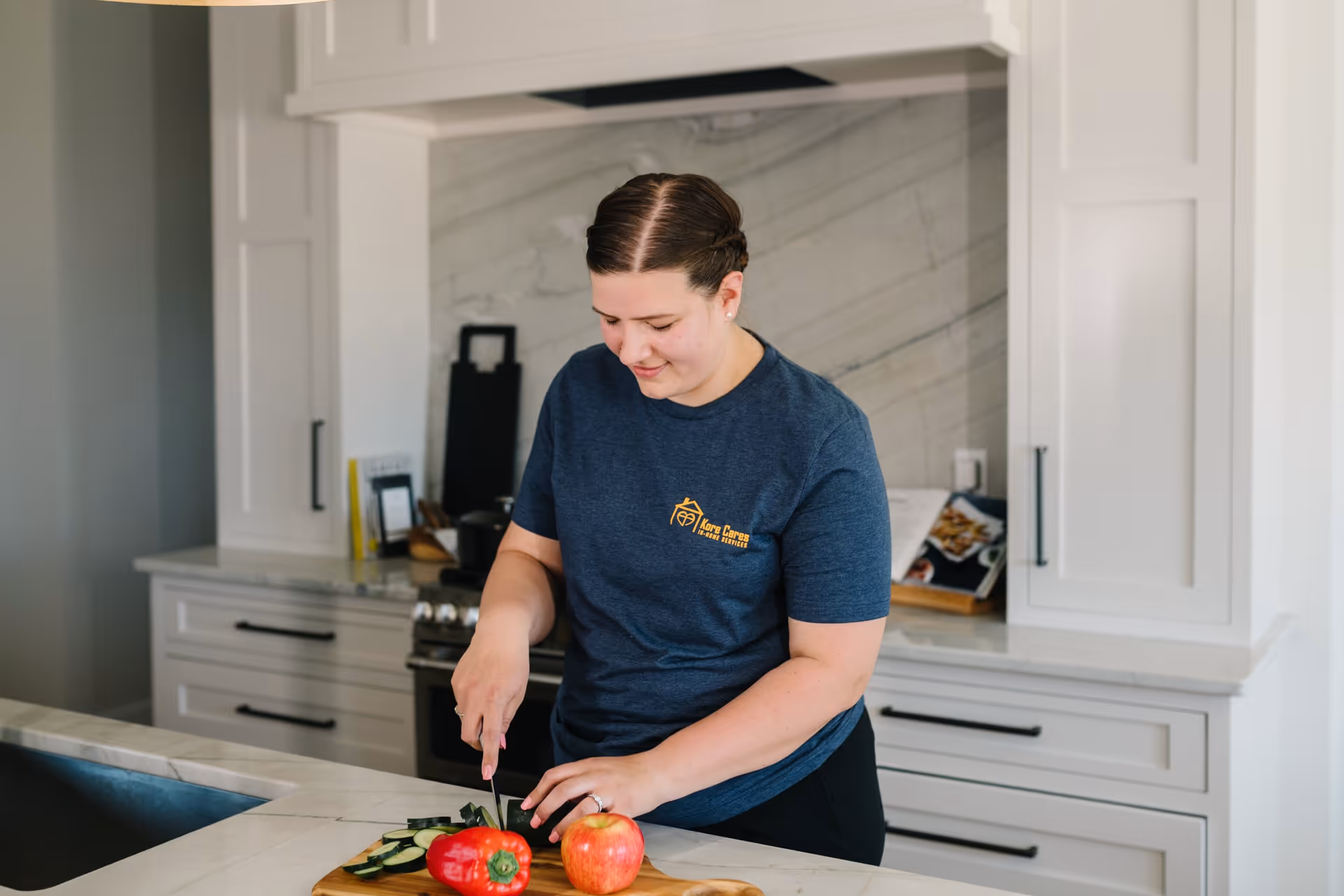 A woman wearing a Kore Cares shirt chops vegetables on a kitchen island.