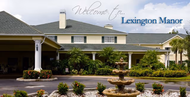 Exterior view of Lexington Manor, a large building with a covered entrance, surrounded by greenery and a decorative fountain in the foreground.