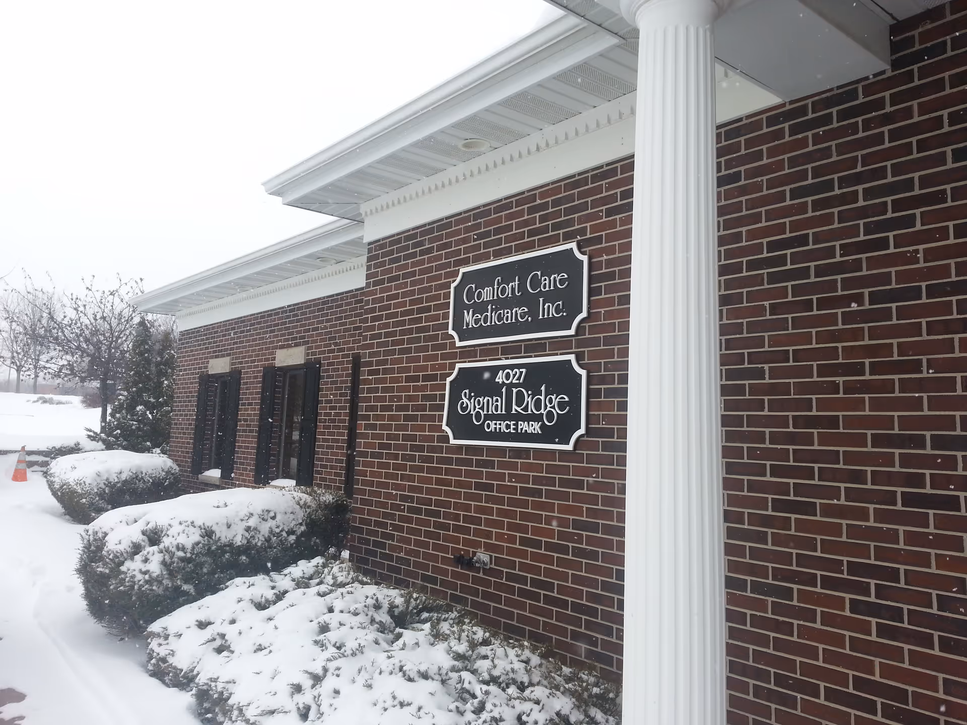 Brick exterior of Comfort Care Medicare, Inc. building with sign plaques in snowy landscaping.