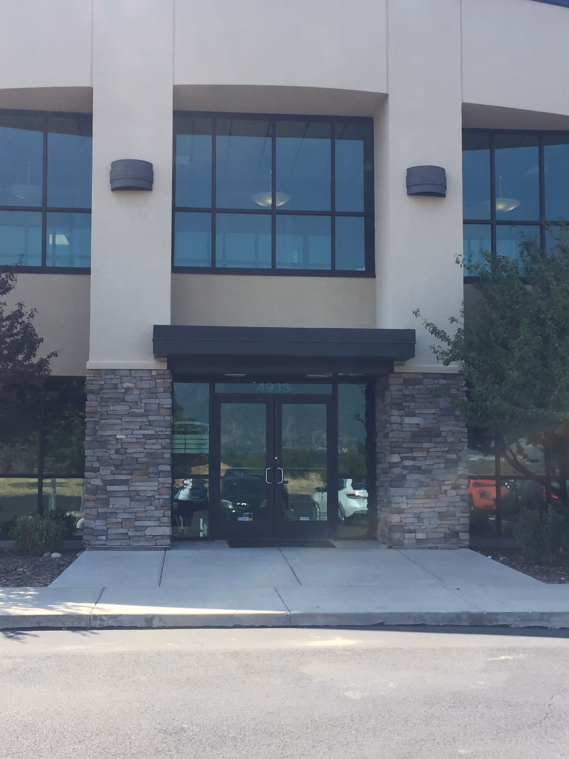 Modern two-story building entrance with glass doors and stone column accents.