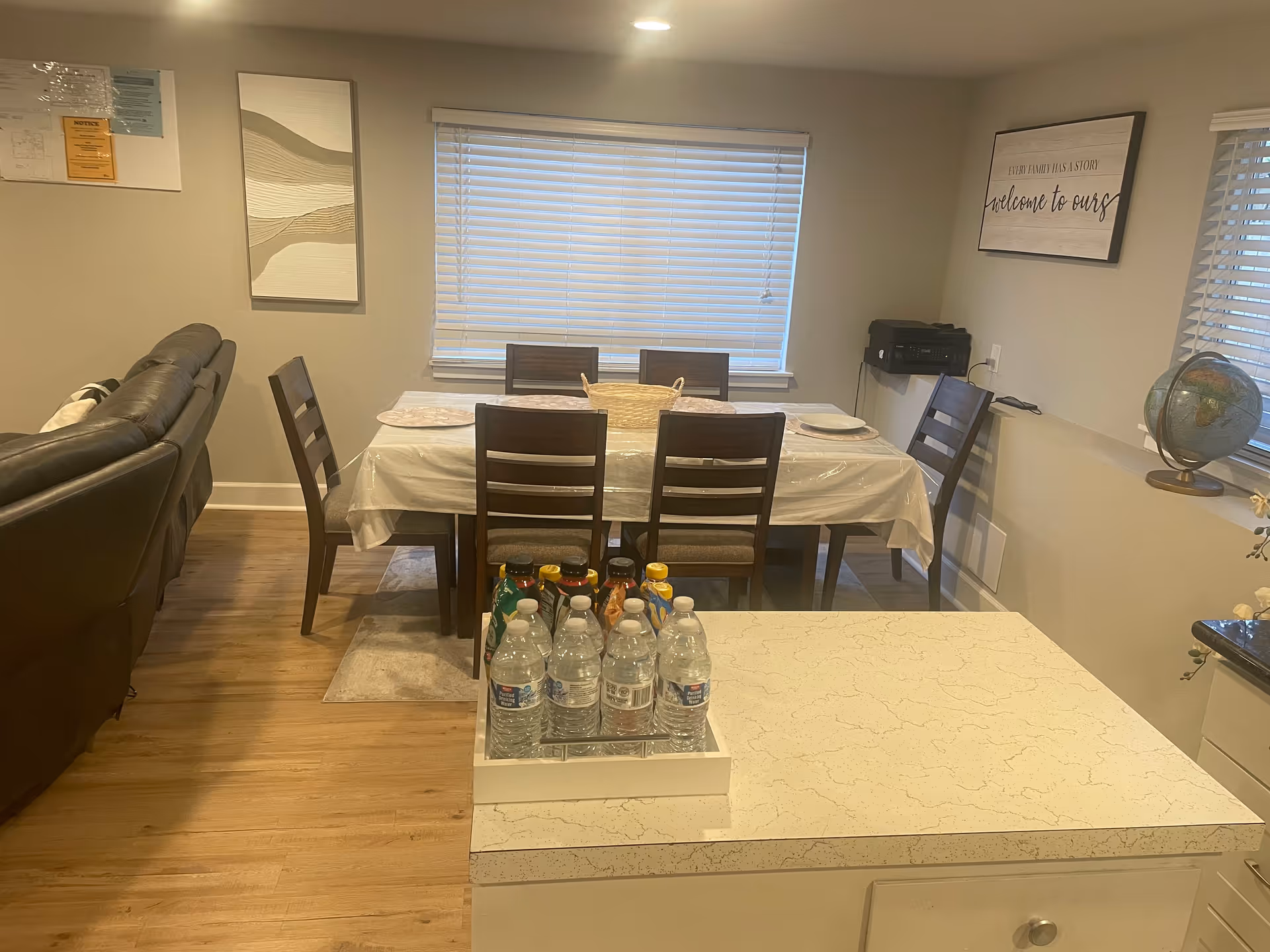 Dining room with table set for six, adjacent living area, and water bottles on counter.