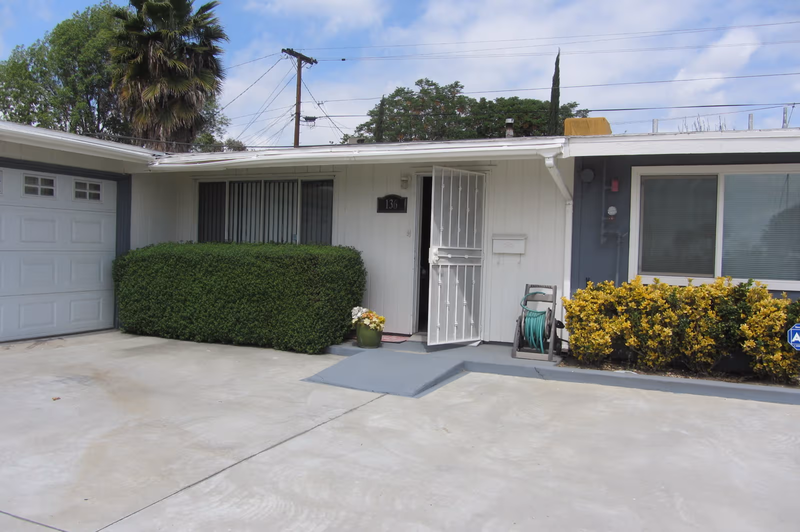 A single-story facility entrance with shrubs, a metal gate, a driveway, and a garage.