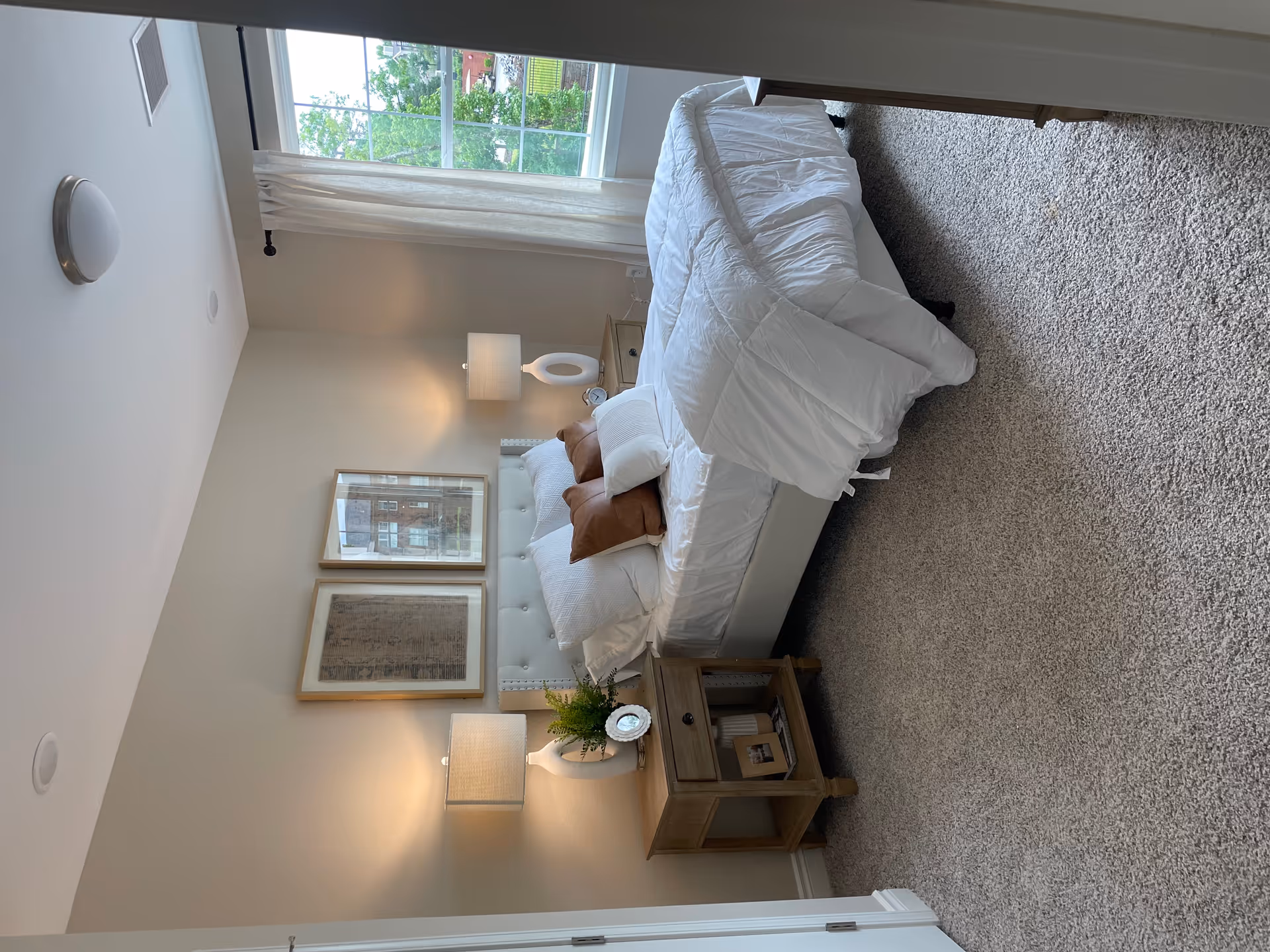 Bright, neatly made bedroom with white bedding, nightstands, lamps, and a window view.
