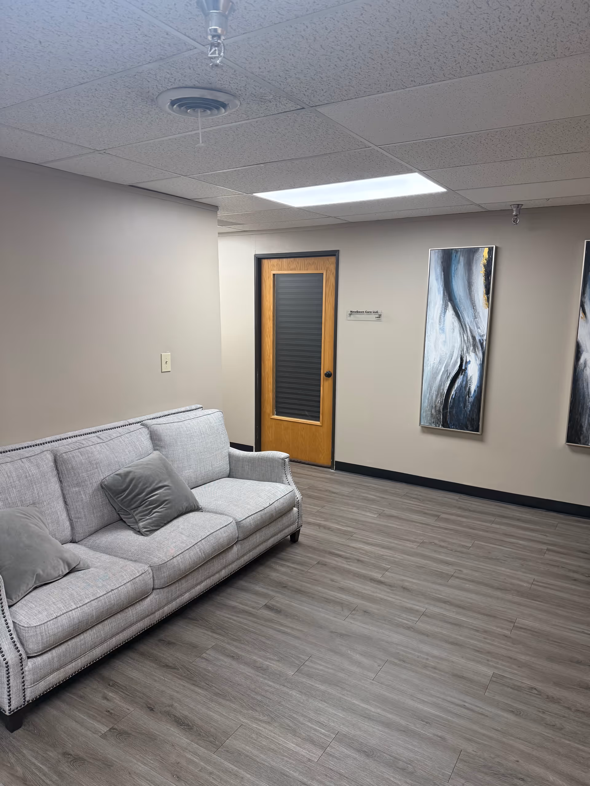 Light gray sofa sits in a modern waiting area with abstract wall art and door.