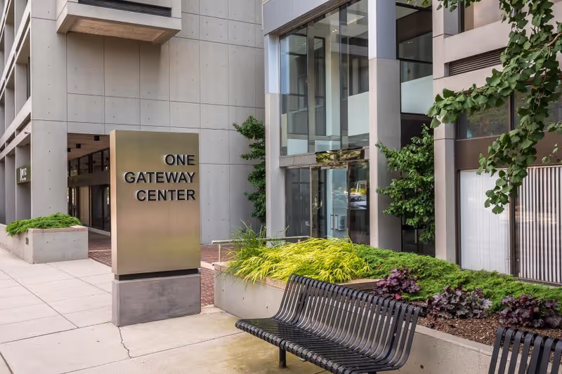 Modern building exterior with bench seating, planters, and a sign reading One Gateway Center.