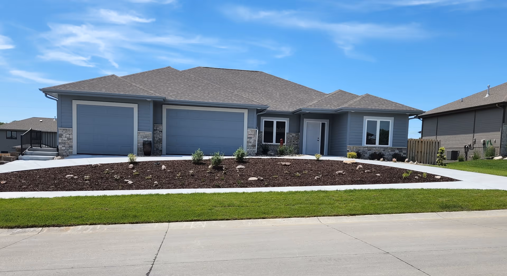 Modern single-story gray home with manicured mulch bed, walkway, and two garage bays.