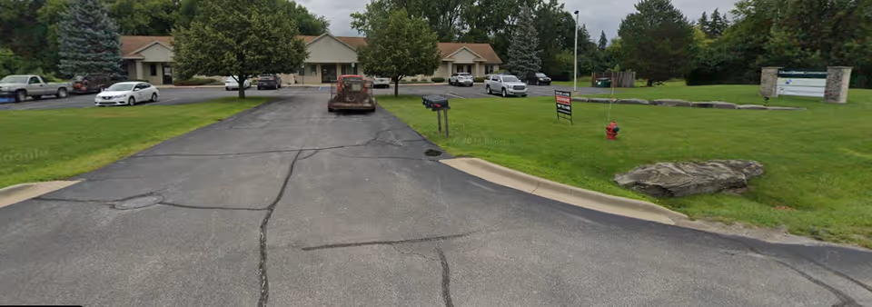 Exterior view of Helping Hand Nursing facility from the driveway with parked cars.