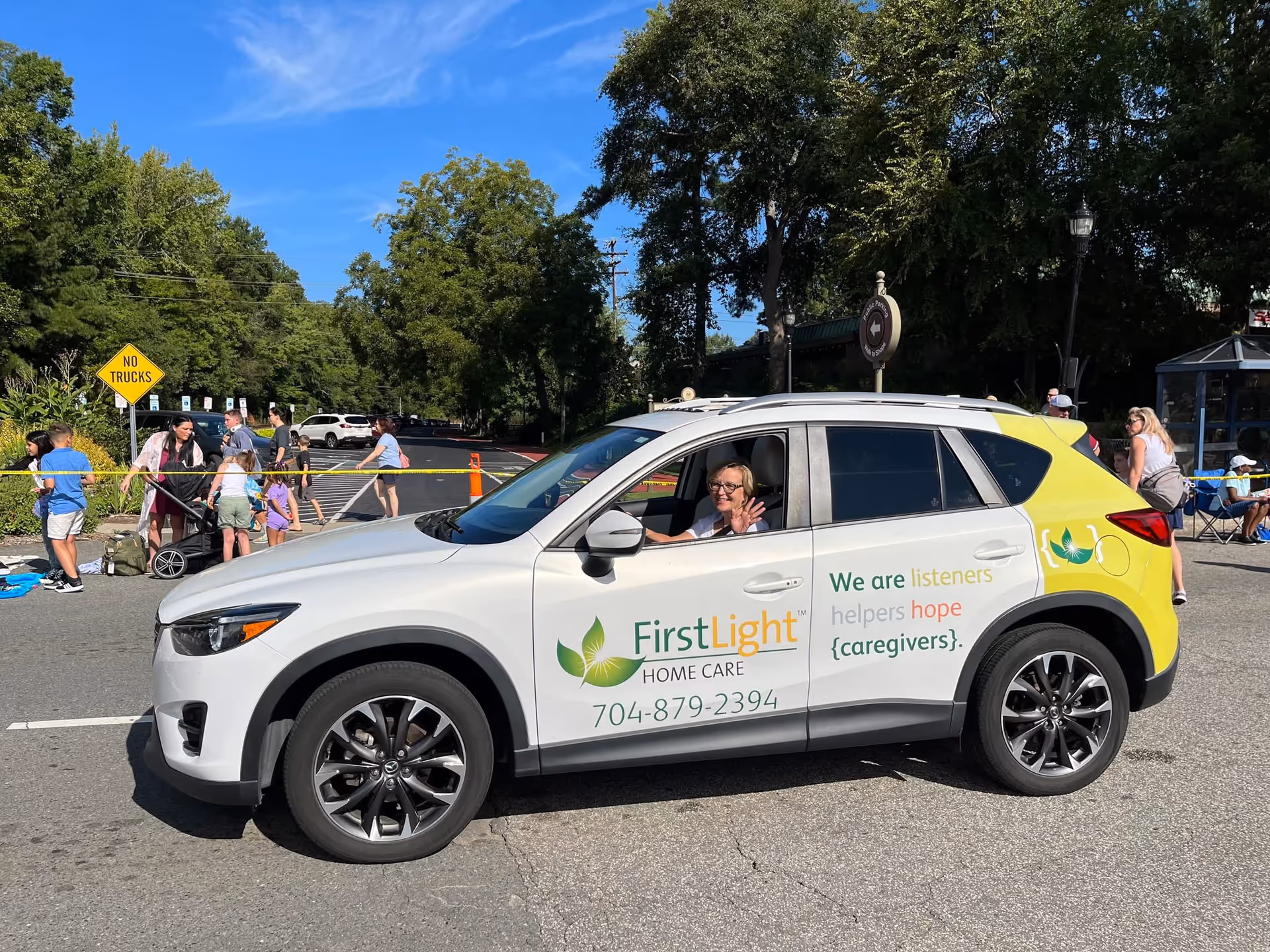 White FirstLight Home Care SUV with a person waving from the driver's seat outdoors.