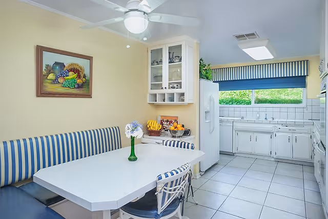 Bright dining area with a white table, blue-striped seating, and a connected kitchen.