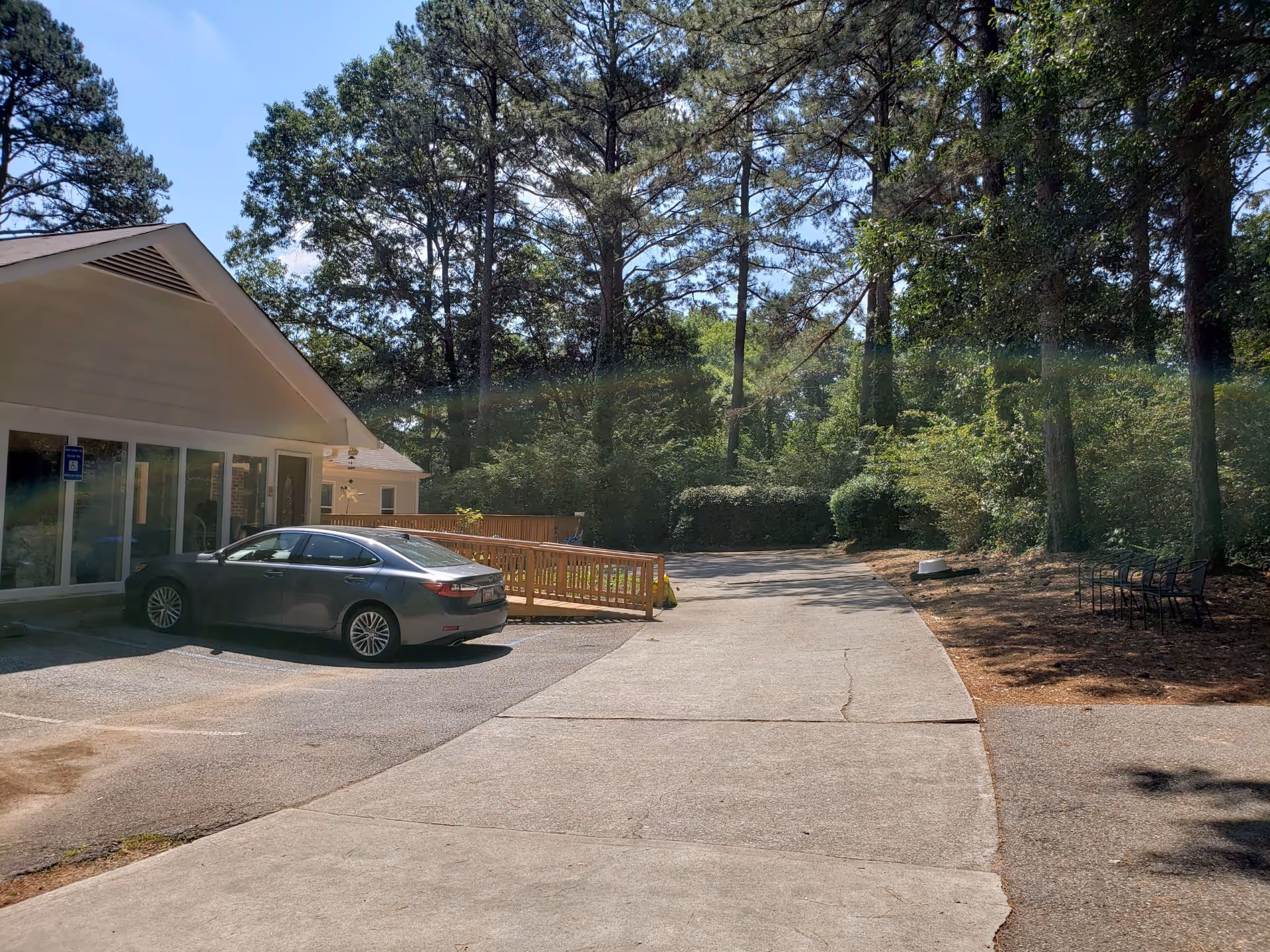 Front exterior of a senior living facility with car, ramp, benches, and trees.