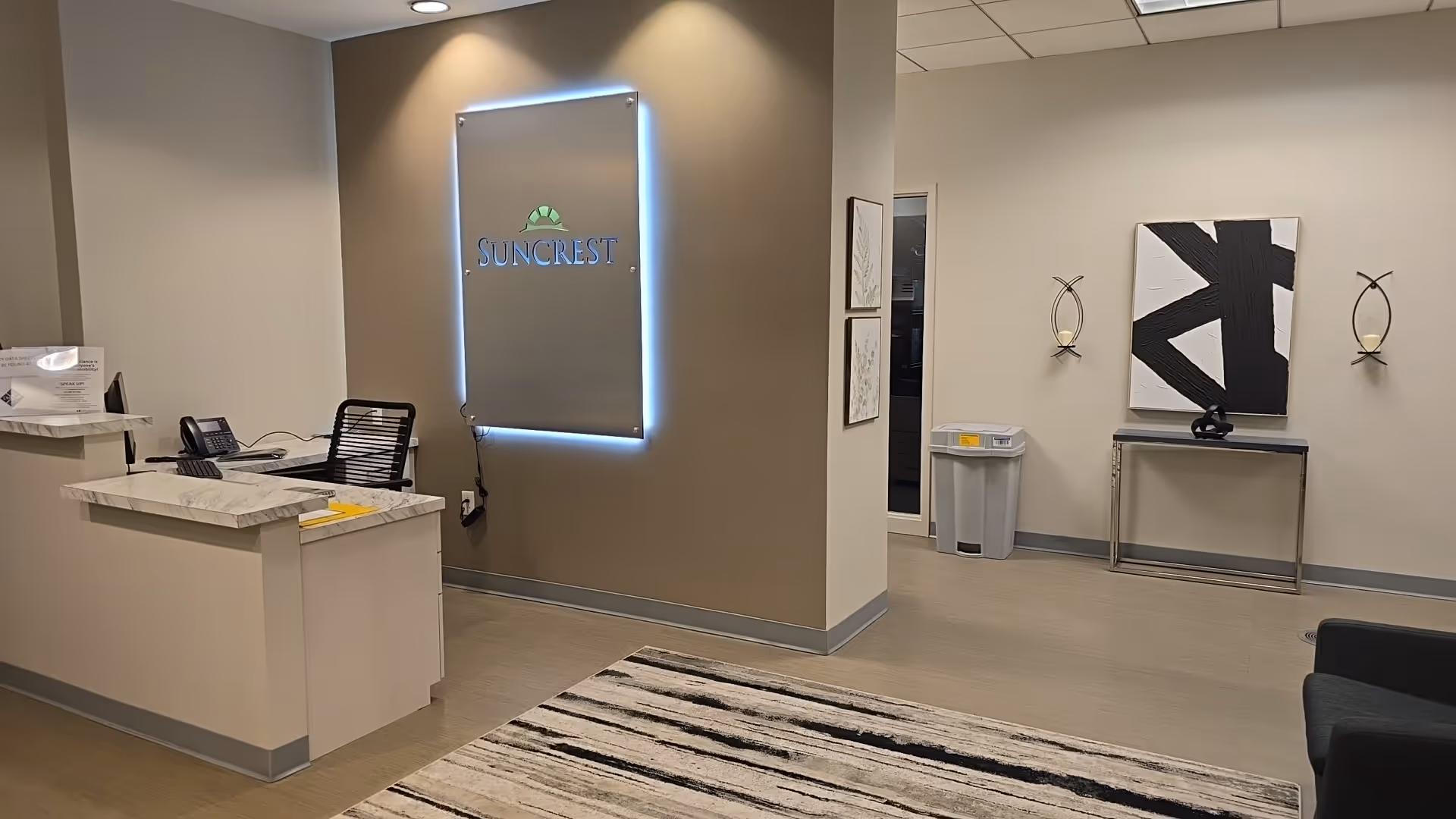 Lobby reception area with Suncrest sign, front desk, abstract art, and seating.