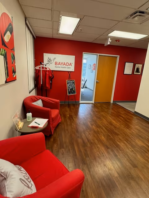 Red-walled indoor reception area with red chairs, BAYADA sign, and doorway to another room.