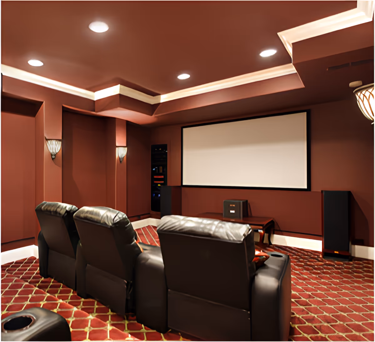 Private home-theater style room with leather recliners facing a large projection screen and speakers on a patterned carpet.