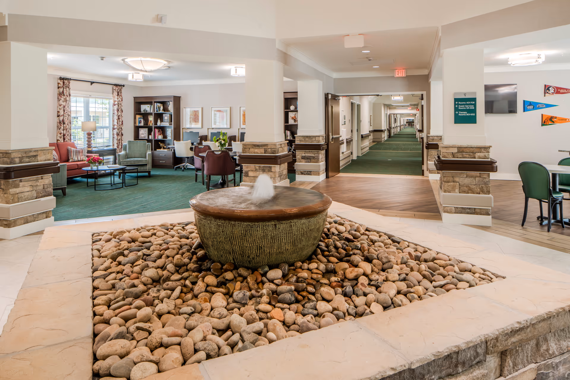 Indoor senior living lobby with rock fountain, seating areas, and a long corridor.