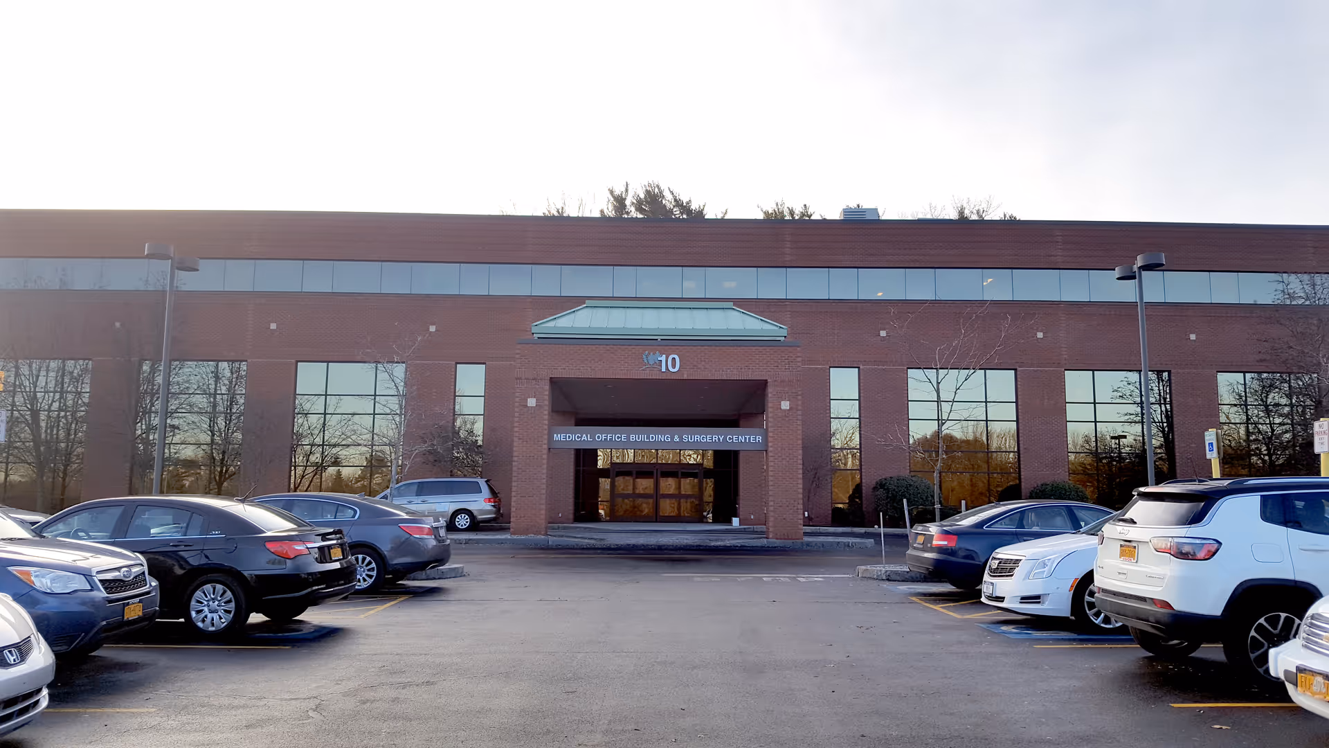 Red brick medical building front with glass doors and a parking lot.
