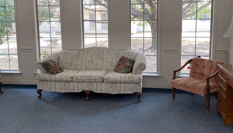 Floral sofa and pink chair sit in a bright sunlit living room with large windows.