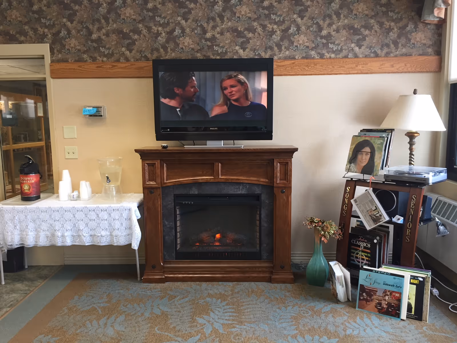 TV over a wooden fireplace mantel in a cozy lounge with magazines.