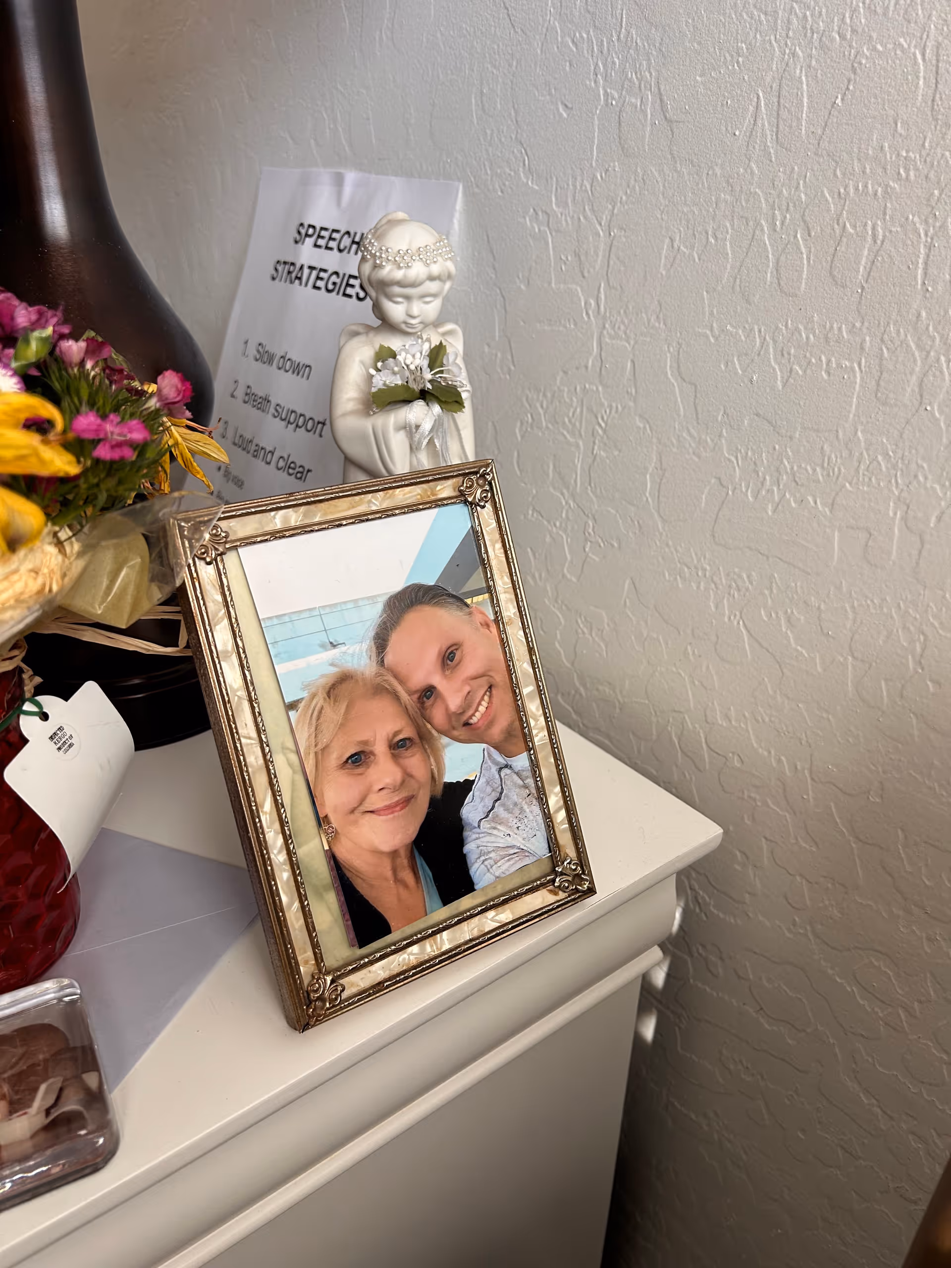 Decorative dresser with a framed photo of two people, flowers, and a small statue.