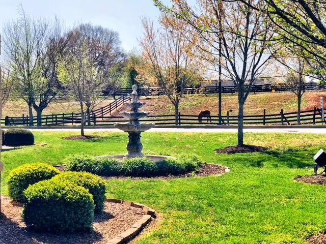 Well-kept outdoor courtyard with a central fountain, trees, and a split-rail fence.