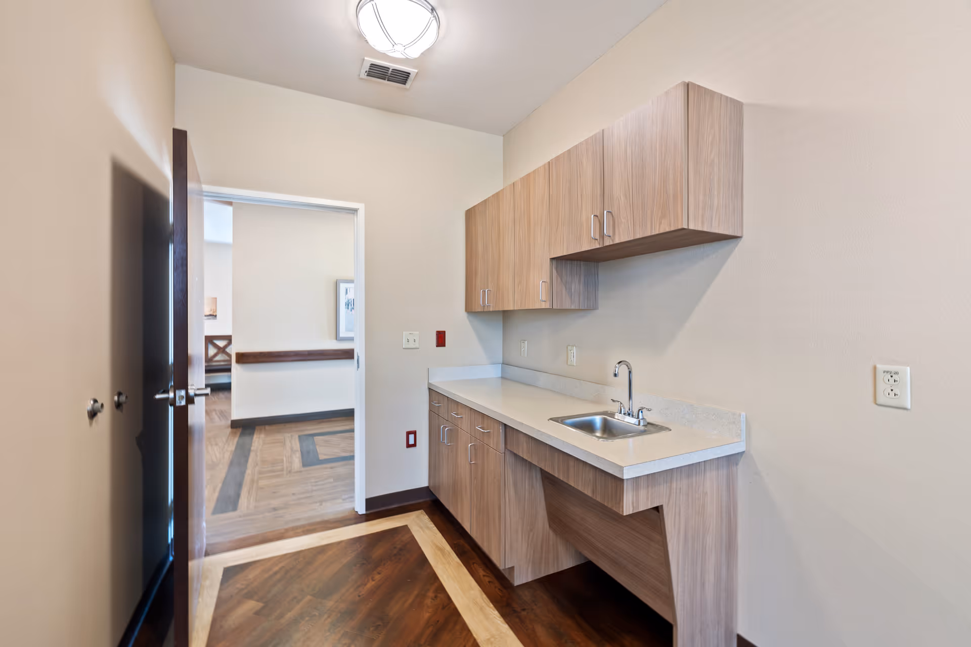 Interior kitchenette with wooden cabinets, sink, and doorway to a hall.