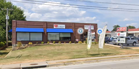 Brick Premier Home Health Care building with blue awnings, signs, and flag banners in front.