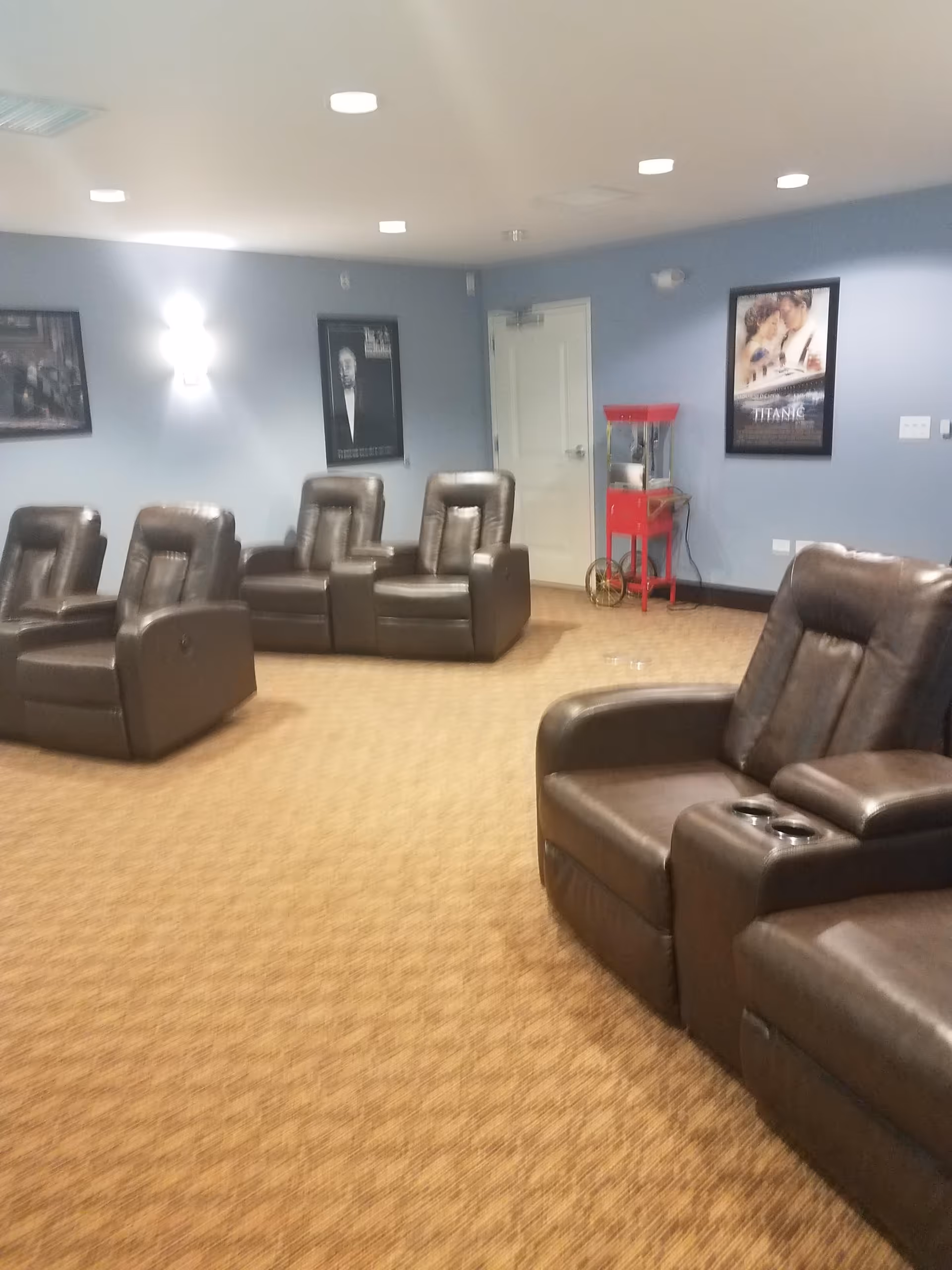 Blue-walled senior living lounge with leather recliners, posters, and a red popcorn cart.