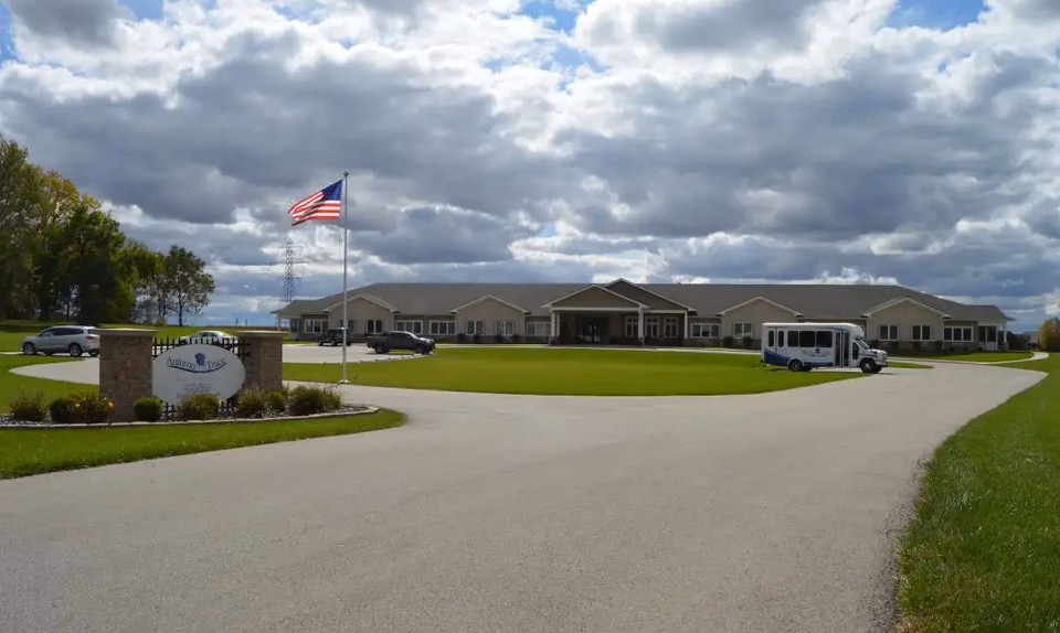 Front exterior of Autumn Trace Attica Assisted Living with flag, driveway, and bus