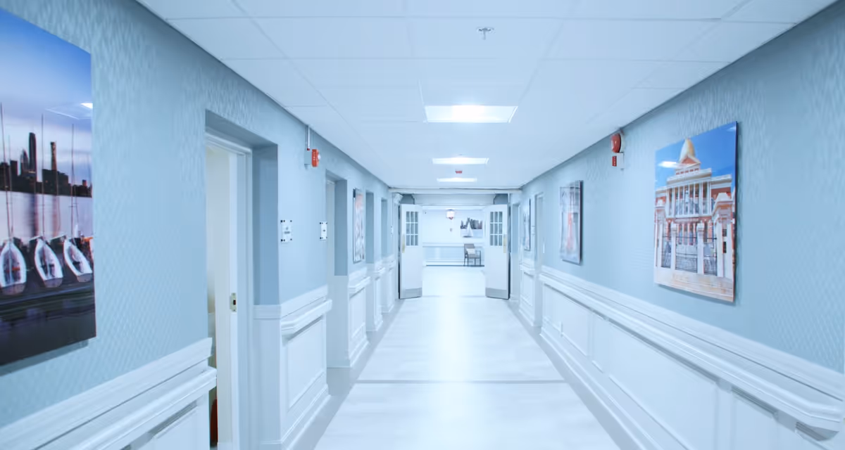 Long blue-walled hallway in a senior living center with framed art along the walls.