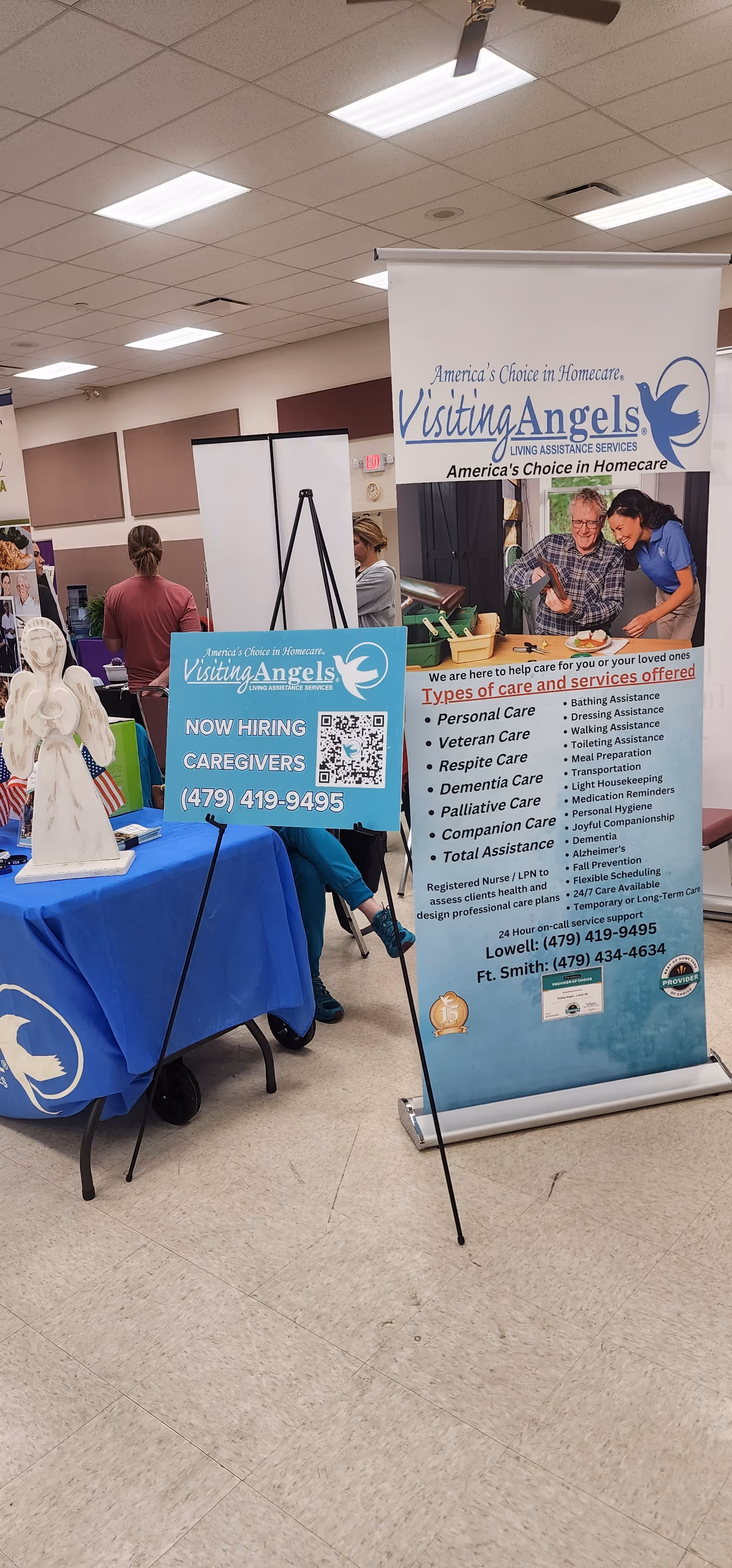 Indoor expo booth for Visiting Angels senior home care with banners and a blue table.