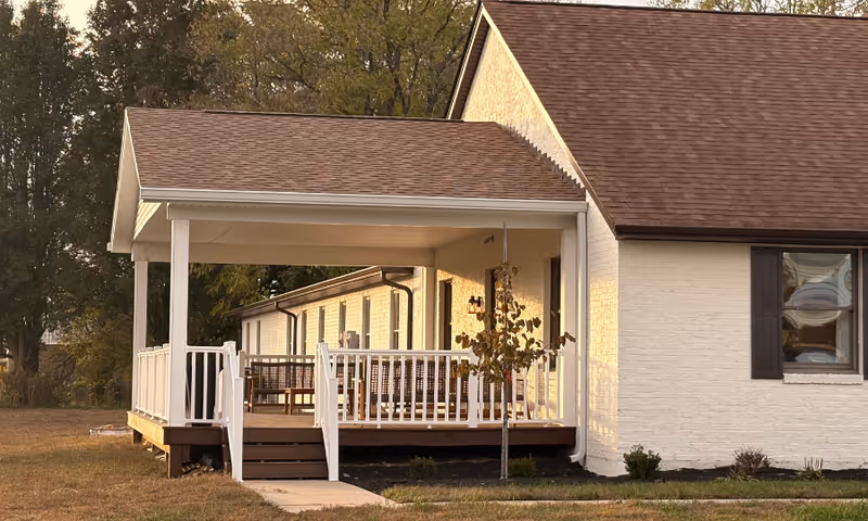 Single-story white-brick senior living facility with a covered front porch and outdoor seating.