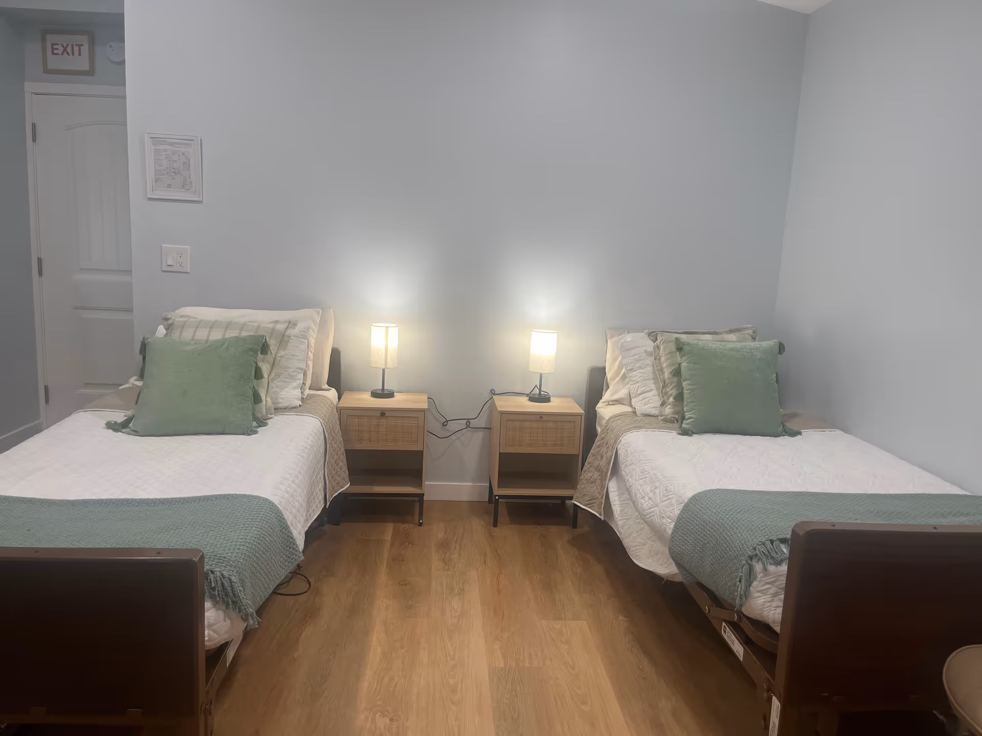 Two single beds with matching bedding flank nightstands with lamps in a tidy bedroom.