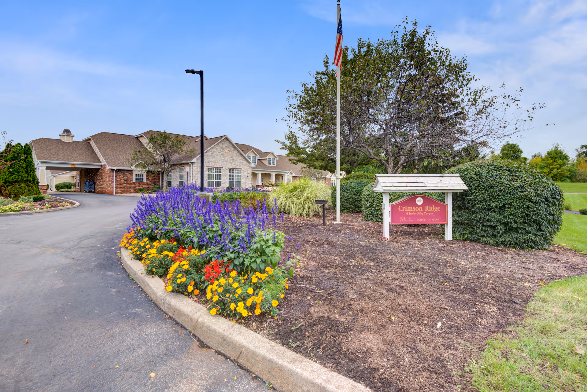 Crimson Ridge Gardens facility front exterior with landscaped flower bed, sign, and flagpole.