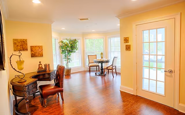 Interior of a sunny senior living room with a bay window, round table and chairs.