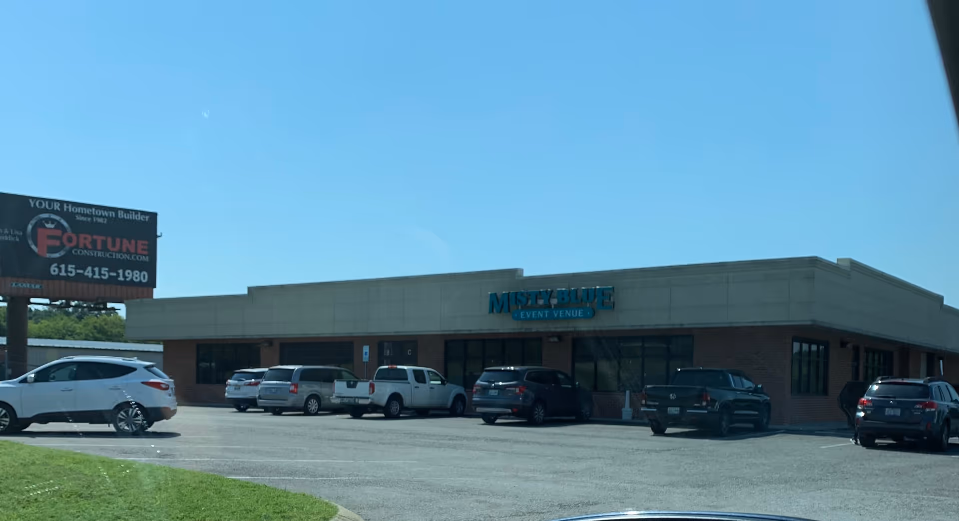 Front exterior of a single-story brick building with several parked cars in the lot.