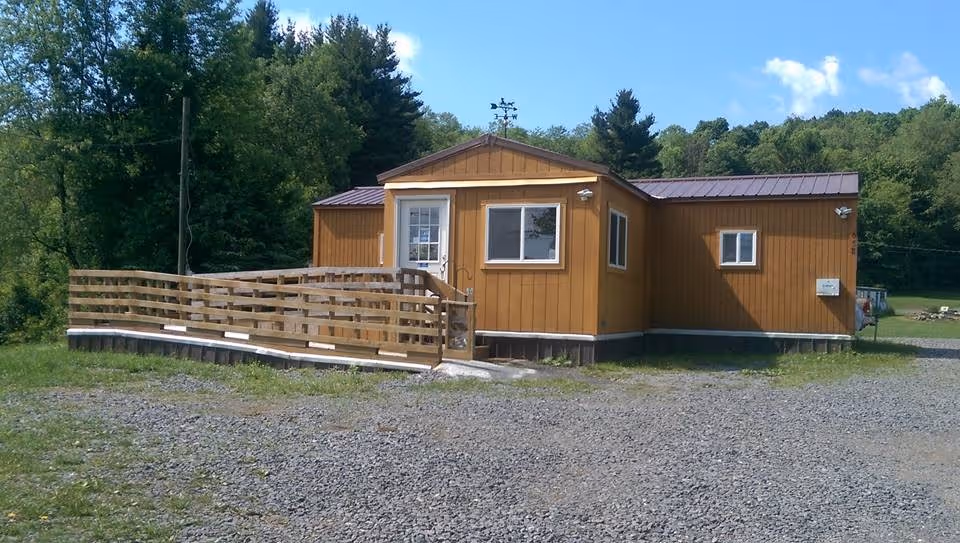 Front exterior of a small brown modular building with a wooden ramp.