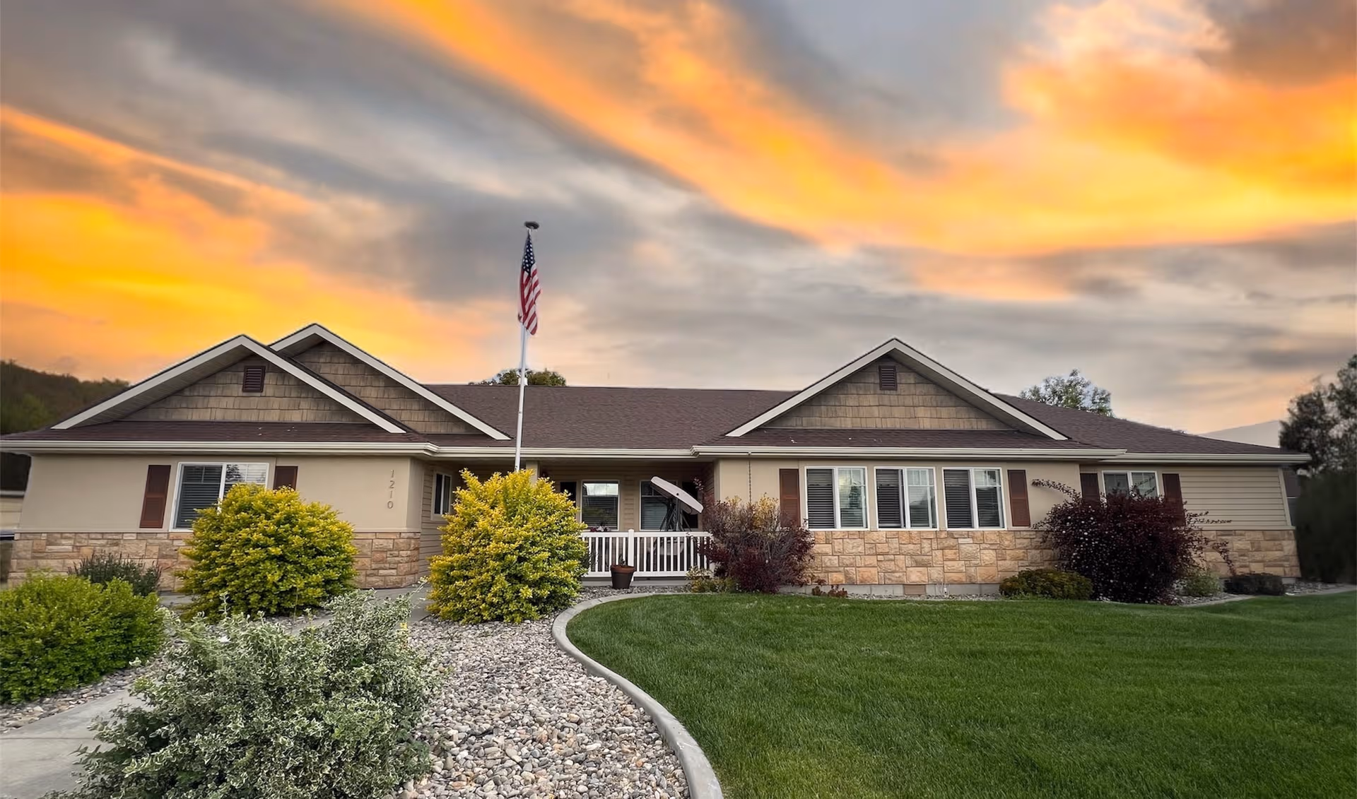 Single-story memory care facility exterior with manicured lawn and flagpole at sunset.