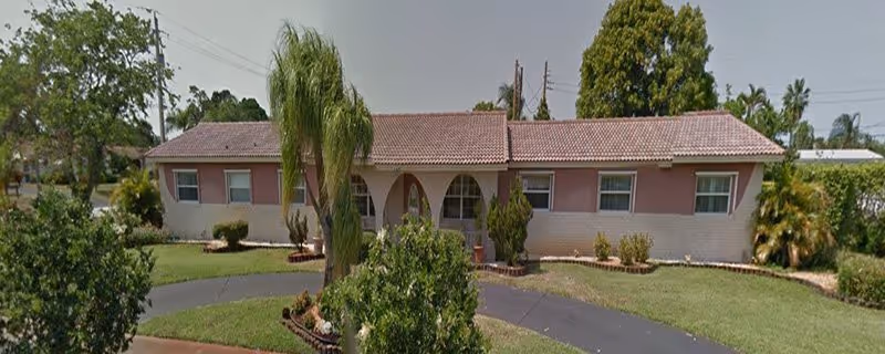 Single-story pink facility facade with arched entrance and palm trees in a landscaped front yard.