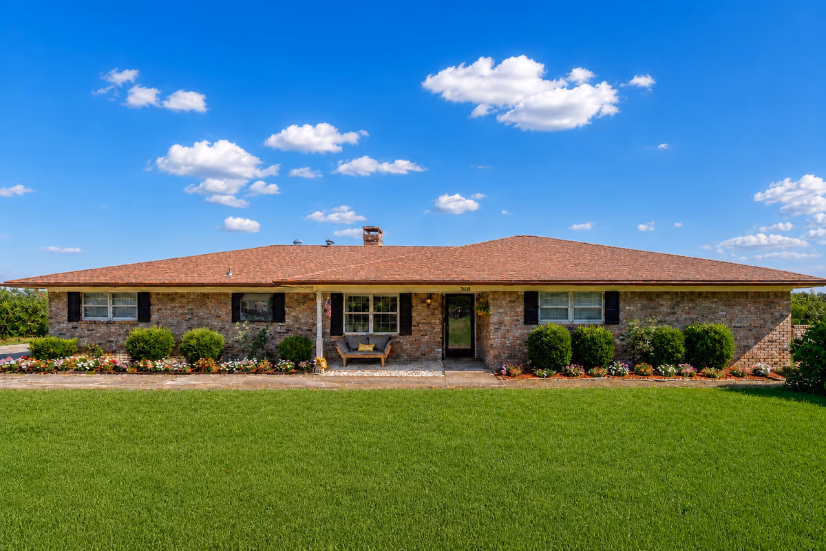 Single-story brick senior facility exterior with manicured lawn and flower beds.