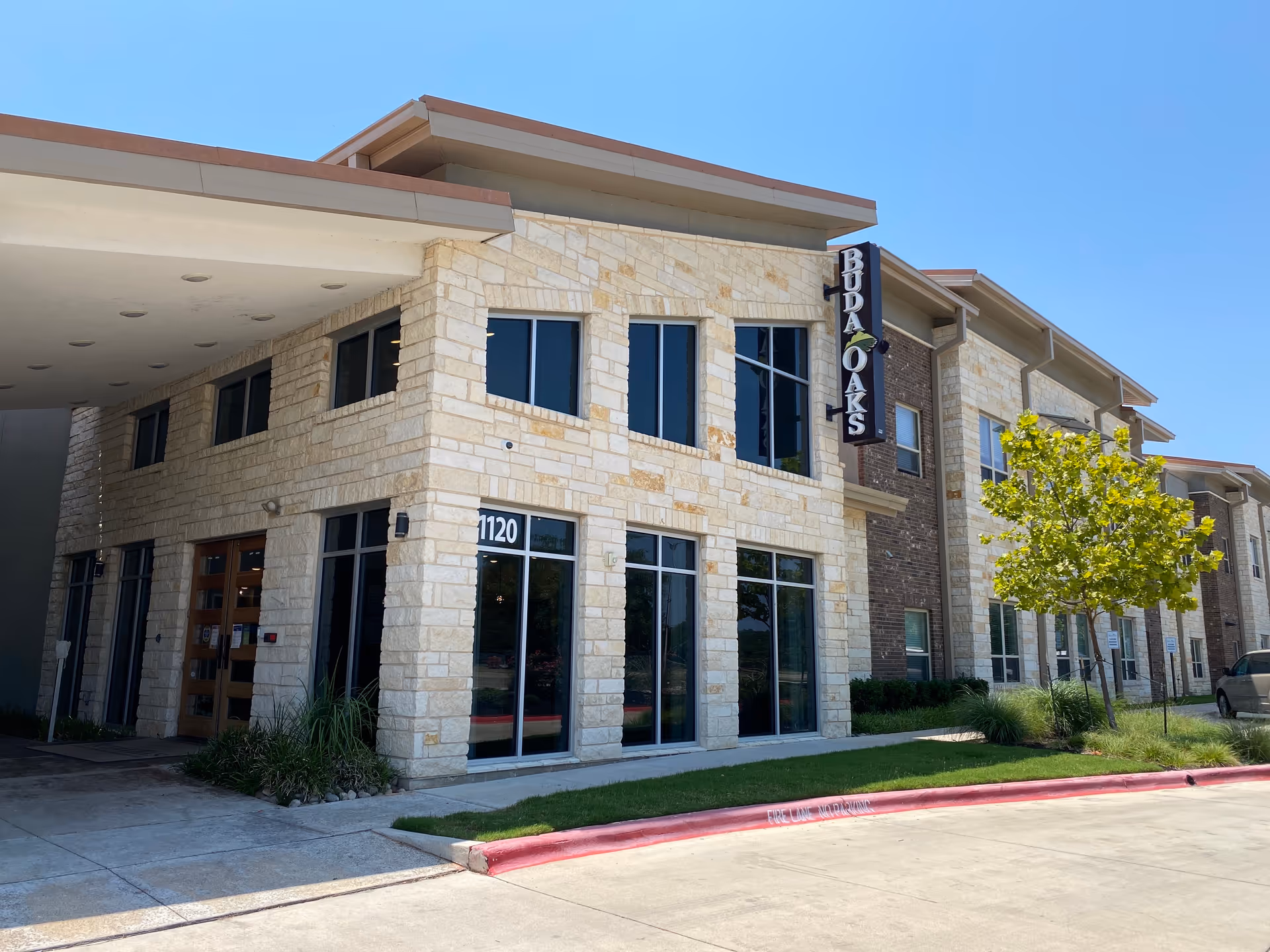 A stone exterior of a senior living facility with a Buda Oaks sign and glass entrance.
